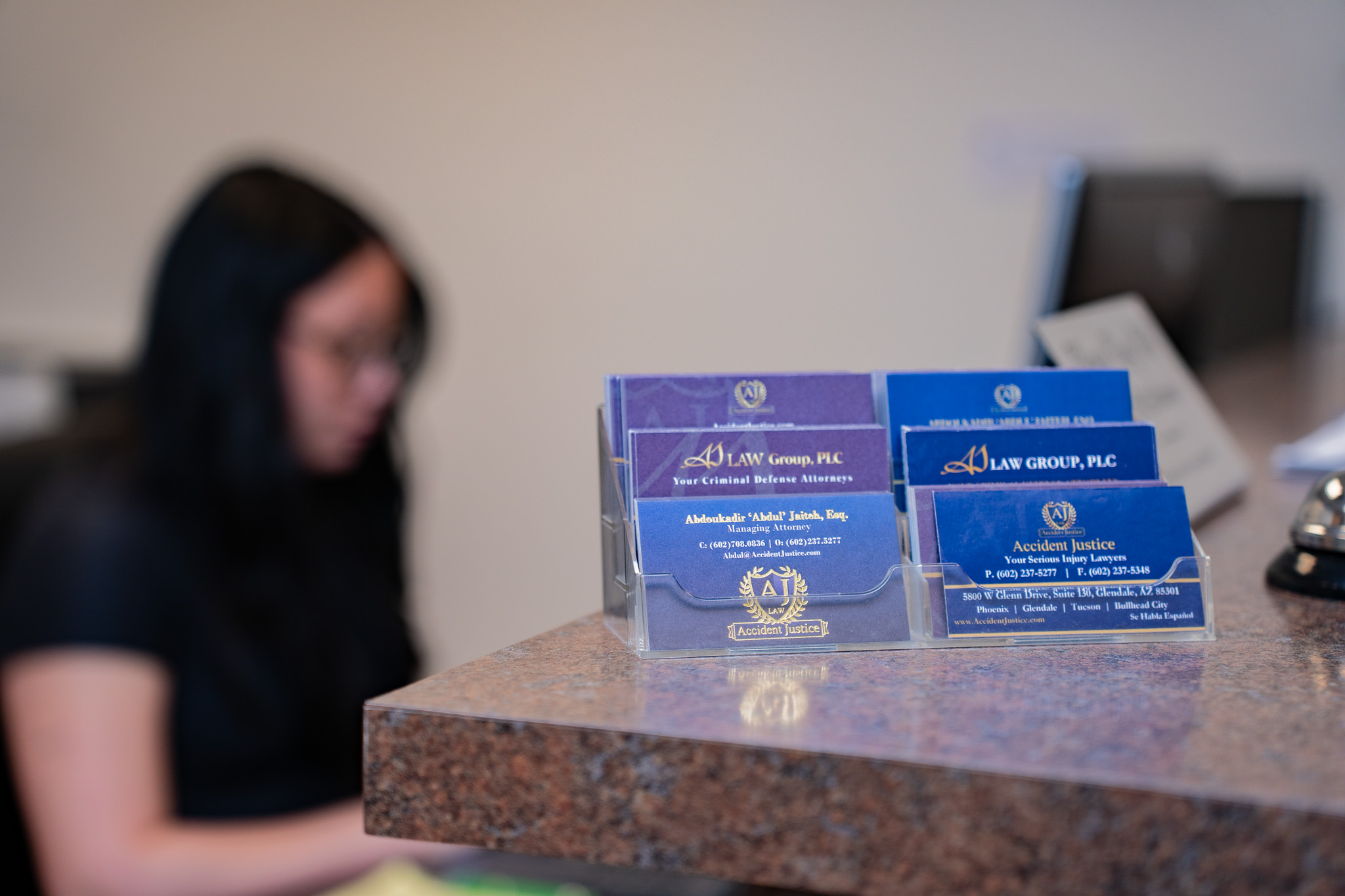 Business cards for Accident Justice and AJ Law Group, PLC displayed at a law office reception desk, with a blurred receptionist in the background.